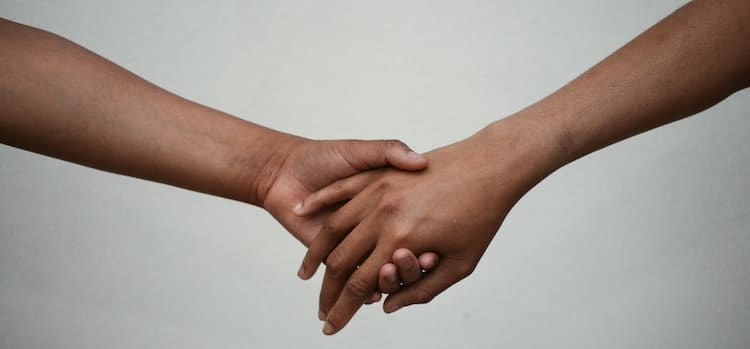 kaksi toistaan pitelevää kättä vaalealla taustalla